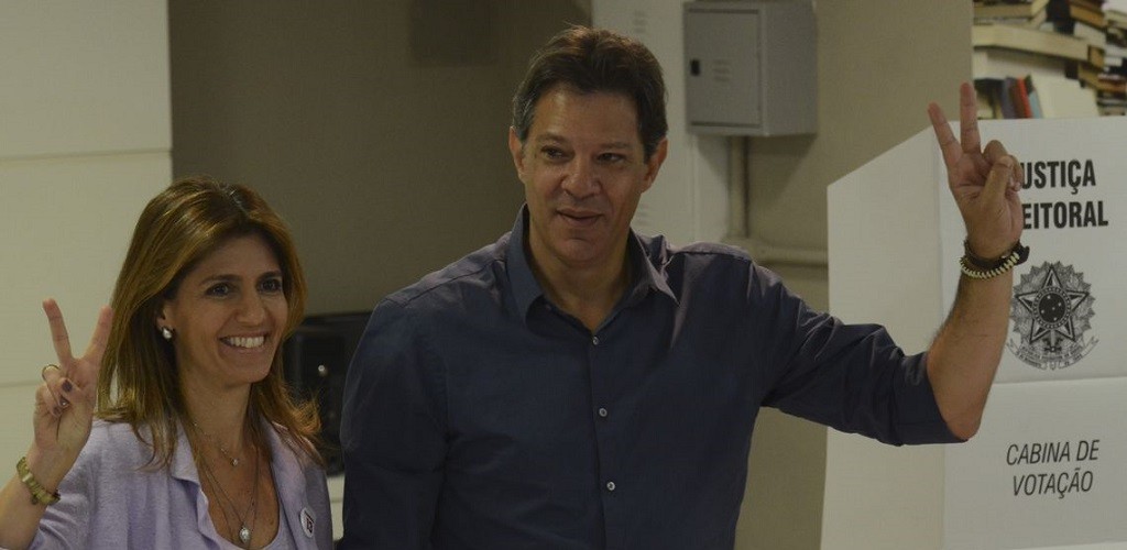 Com camisa azul, Haddad vota e faz sinal de vitória